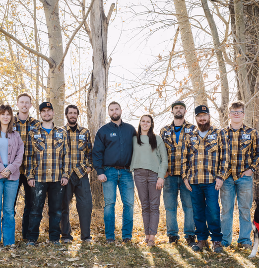 A diverse team of men and women from Icon Industrial standing together outdoors in a grove of trees, wearing branded apparel.