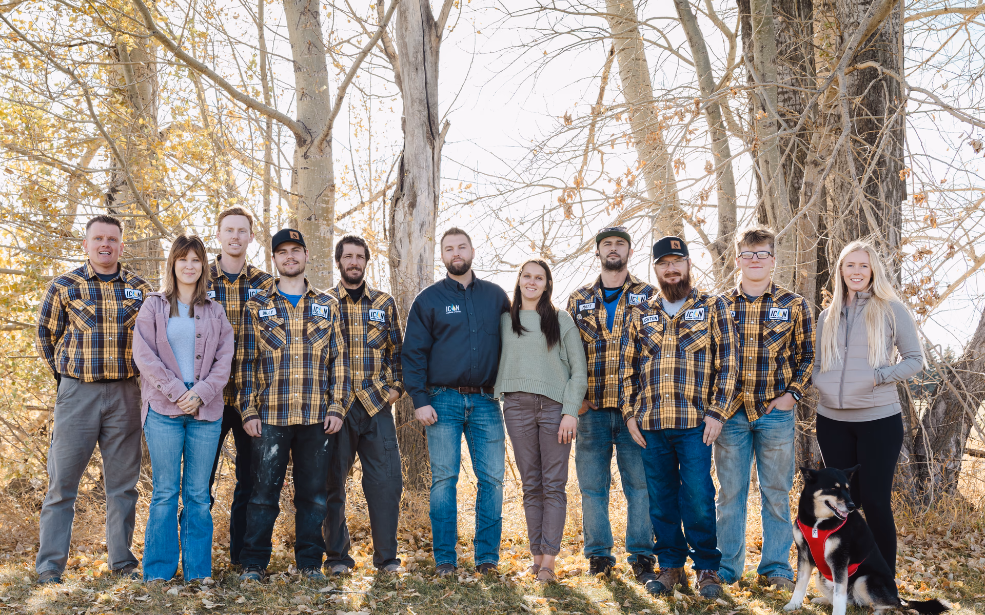 The team from Icon Plumbing & Heating, consisting of men and women in casual workwear, posing together outdoors by trees.