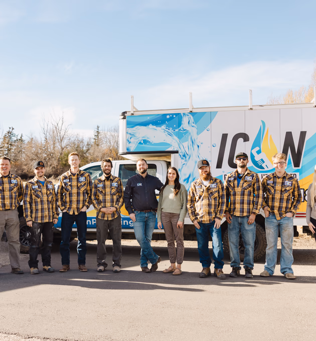 The ICON Plumbing team, consisting of eight men and one woman, stands together in front of a branded company work truck.