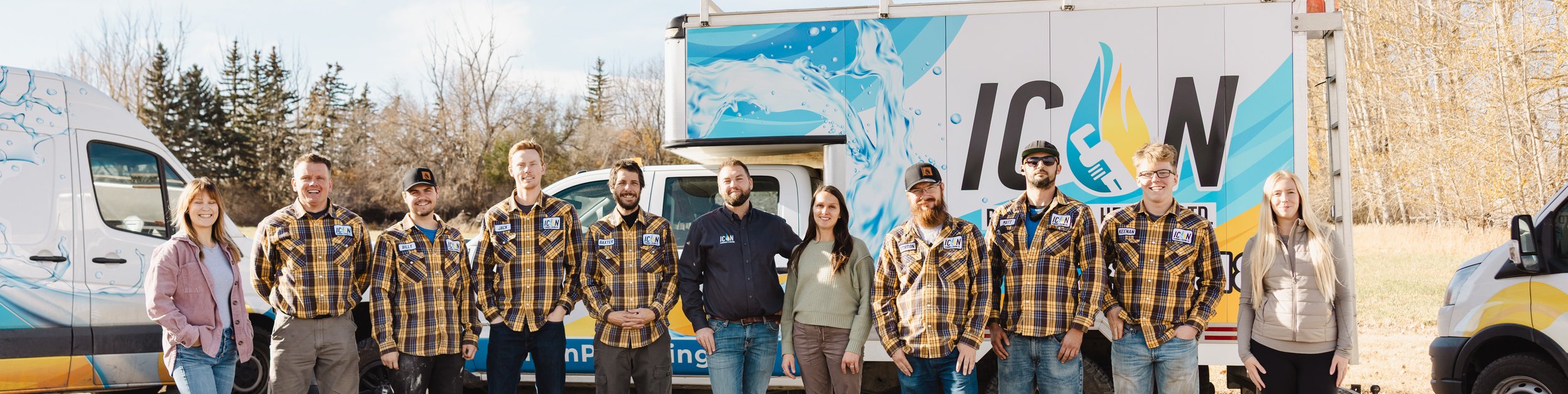 The ICON Plumbing and Heating team stands in a line outdoors in front of their branded work vans, wearing company gear.