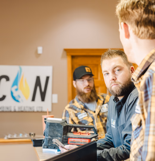 Three workers from C&N Plumbing & Heating Ltd. discuss business in an office setting, with one checking a mobile device.