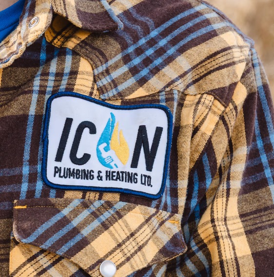 A brown and yellow plaid flannel shirt with a patch reading ICON PLUMBING & HEATING LTD and a blue and yellow flame icon.