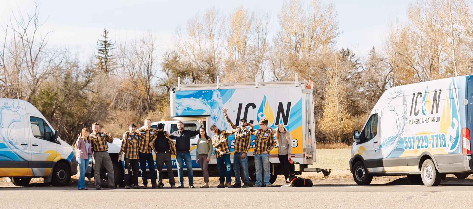 The Icon Plumbing & Heating team standing together outdoors in front of branded company trucks, some wearing plaid shirts.