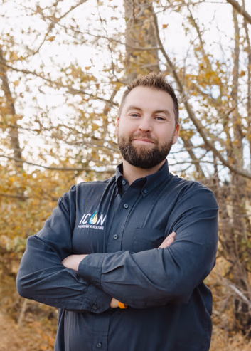 Bearded man wearing a dark button-down shirt with an Icon Plumbing & Heating logo, posing outdoors with arms crossed.