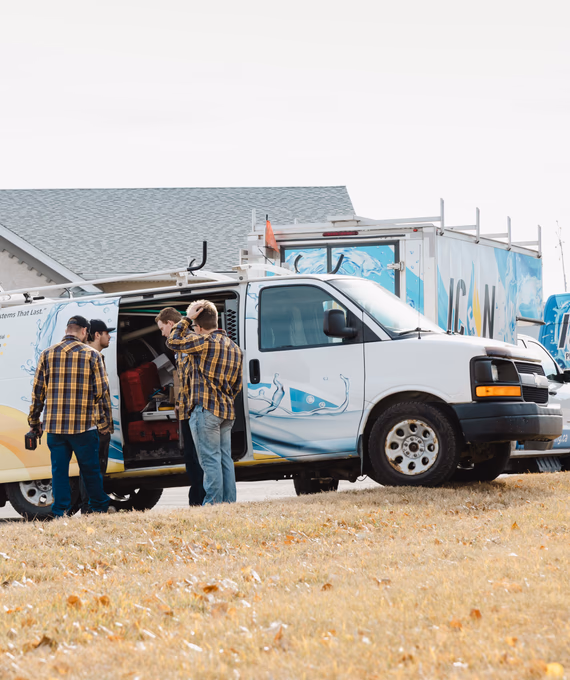 Three tradespeople in yellow plaid shirts and jeans stand outside their white service van labeled "ICON" to organize tools.